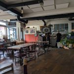 Rustic interior of a cafe with wooden tables, exposed ductwork, and a service counter.
