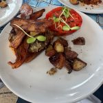 Plate of crispy bacon, roasted potatoes, and a tomato slice with greens.
