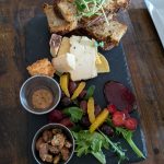 Cheese board with bread, crackers, cured meats, and fresh greens on a slate platter.