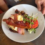 Breakfast plate with bacon, egg, and tomato on toast, set on a wooden table.