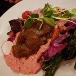Gourmet plate with pink puree, rich brown sauce, microgreens, and roasted vegetables.
