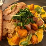 Plate of sliced meat, roasted potatoes, greens, and a yellow sauce.