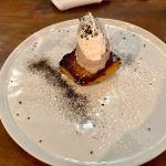 Dessert featuring a scoop of ice cream on a warm, dark base, dusted with powdered sugar and cocoa.