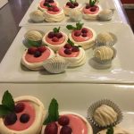 Assortment of small, decorated pastries and desserts on white serving platters.
