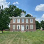 Historic brick house with white trim and cupola under a blue, cloudy sky.