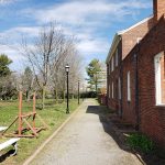 Brick building alongside a pathway with trees and open green space under a blue sky.