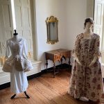 Mannequins display vintage white and floral dresses in a bright, antique-styled room.