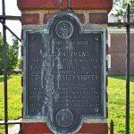 Historical plaque on a brick pillar detailing the house's construction and restoration.