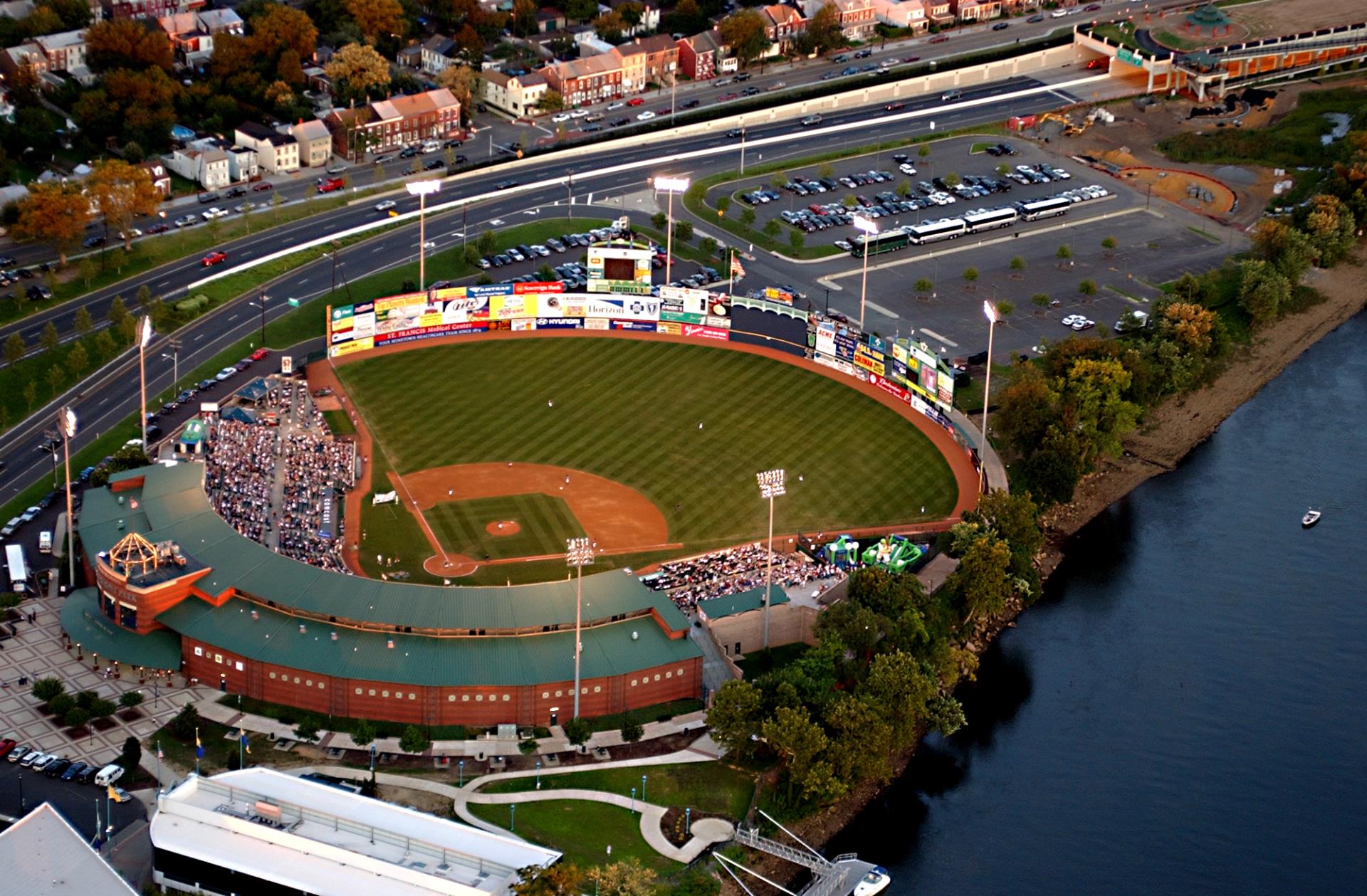 Baseball stadium overlooking a river and city skyline during a game.