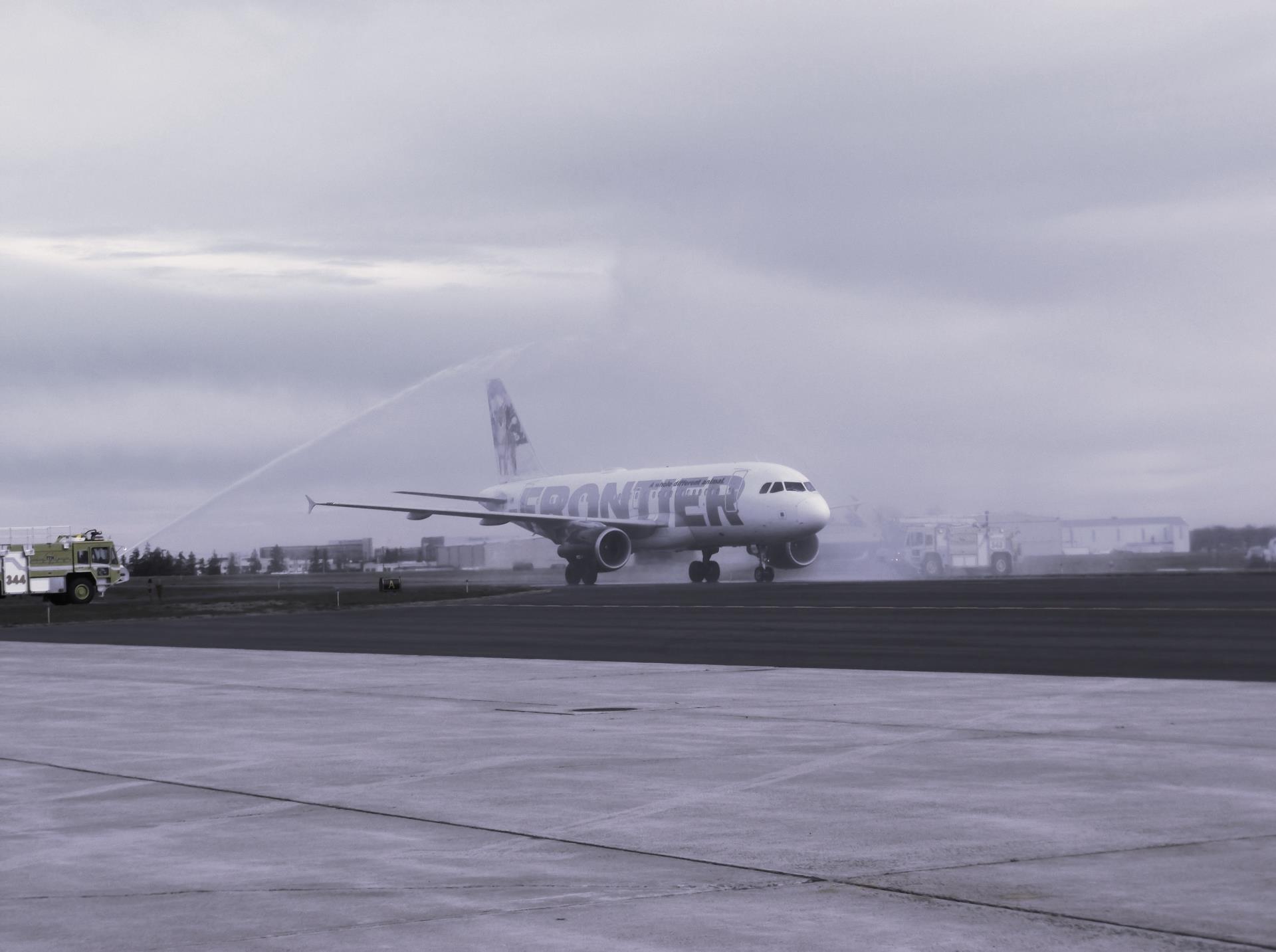 Frontier jet taking off on a wet runway under an overcast sky.