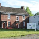 Historic brick house with white trim and lawn, featuring a welcome sign.