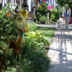 Colorful, stylized goat sculpture in a park setting with a paved walkway.