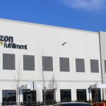 Amazon fulfillment center exterior under a bright blue sky.