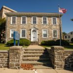 Historic stone building with columns and American flag under a clear blue sky.