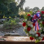 Floral arrangement with patriotic ribbon against a backdrop of lush greenery and rocks.