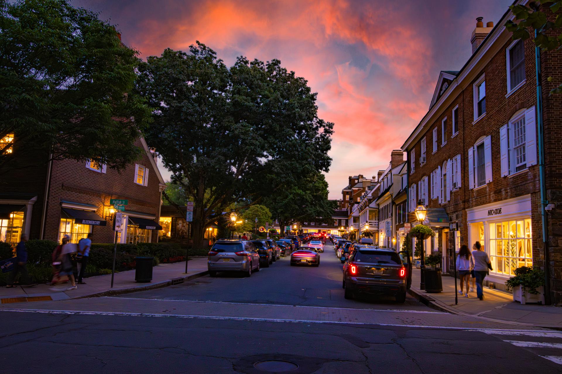 Sunset over a quaint, historic street lined with brick buildings and trees.