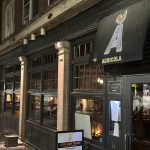 Exterior view of a dark-fronted bar named Agricola at night.