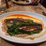 Seared fish fillet with asparagus, white beans, and orange sauce on a white plate.