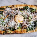 Gourmet pizza topped with spinach, mushrooms, cheese, and a dollop of ricotta on a wooden board.