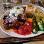 Plate of savory meat dish topped with cheese, served with toasted bread and fresh lettuce.