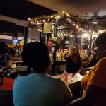 Group of people socializing in a dimly lit bar or restaurant setting.
