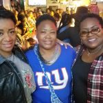 Three smiling women posing together in a crowded, lively indoor venue or bar.