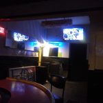 Dark interior of a bar or venue with multiple screens showing video content.