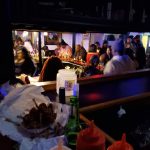 Nighttime bar scene with patrons gathered around a dimly lit counter.