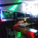 Bar interior with neon lighting, TVs displaying visuals, and a wooden counter.