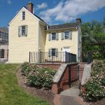 Yellow historic house with green shutters and front garden on a sunny day.