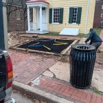 Man working near a black star design in a brick courtyard outside a yellow building.