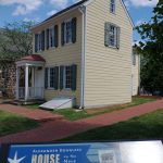 Historic yellow house on the move, displayed outdoors with informational sign.