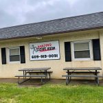 Exterior of a building with an "Amazing Escape Room" sign and picnic tables in front.