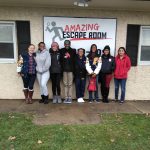 Group of people posing in front of an "Amazing Escape Room" sign.