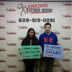 Woman and man pose in front of an "Amazing Escape Room" banner with the number 609-919-0091.