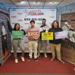 Group of five people celebrating success in an escape room setting with a banner behind them.