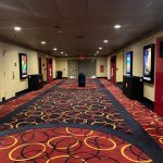 Hotel hallway with patterned red and black carpet, featuring artwork on walls.