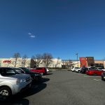 Parking lot view of a commercial building under a clear blue sky with several cars parked.