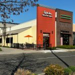 Qdoba Mexican Grill storefront with outdoor seating under a clear blue sky.