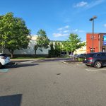 Parking lot view of a modern commercial building under a bright blue sky.