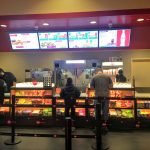 Fast food counter with digital menu boards and various snack displays.