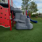 Colorful playground equipment featuring a gray rock climbing structure on green turf.