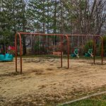 Metal swing set in a grassy backyard with trees and winter foliage surrounding it.