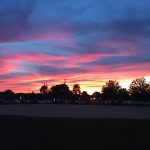 Vibrant sunset with pink and purple clouds over a dark silhouette of trees and horizon.