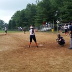 Baseball game in progress on a dirt field with players and spectators visible.