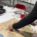 Person sorting old newspapers on a white table in an indoor setting.