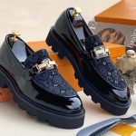 Black patent leather Louis Vuitton loafers with gold hardware, displayed near branded packaging.