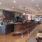 Ice cream shop interior with wooden counter, display cases, and customers.