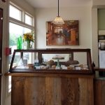 Wooden counter display case with pastries and a vintage bar scene artwork above.