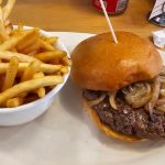 Golden french fries and a cheeseburger with caramelized onions on a white plate.